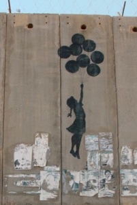 graffiti of a girlchild holding on to a bunch of balloons, which are carrying her over the wall the graffiti is painted on